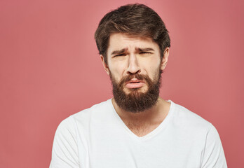 Fototapeta premium Portrait of an upset man in a white t-shirt on a pink background cropped view