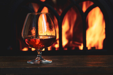 A glass with cognac in front of the fireplace in the cozy living room.