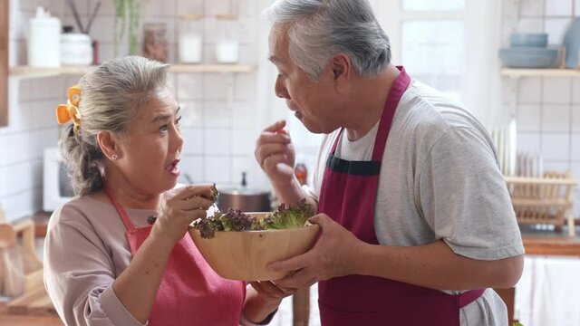 Happy Asian elderly family eating at home. Smiling senior couple enjoy cooking together in the kitchen. Retirement family husband and wife having fun leisure activity lifestyle at home with happiness