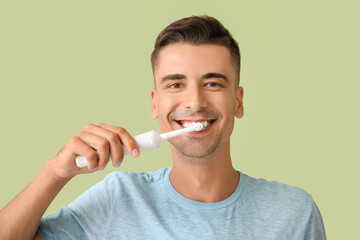 Young man brushing teeth on color background