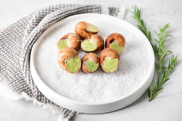 Plate with tasty snails on light background