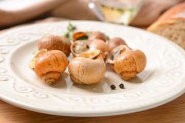 Plate with tasty snails on wooden background, closeup