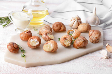 Board with tasty snails on light wooden background