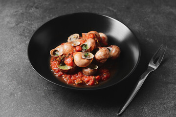 Plate with tasty snails on dark background