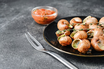 Plate with tasty snails on dark background