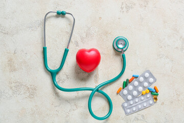 Modern stethoscope, pills and heart on light background
