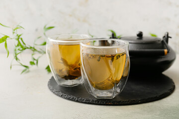 Cups and teapot of green tea on light background