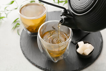 Pouring of green tea from teapot into cup on light background, closeup