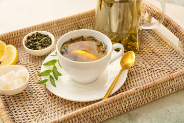 Wicker tray with cup and teapot of green tea on table