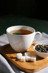 Tray with cup of green tea and dry leaves on dark background
