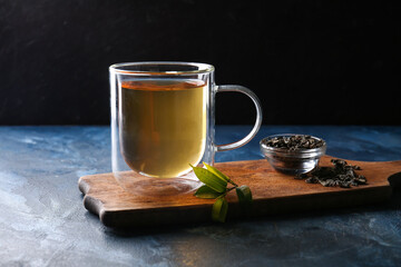 Board with cup of green tea and dry leaves on color background