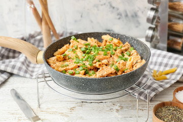 Frying pan with tasty cajun chicken pasta on white wooden background