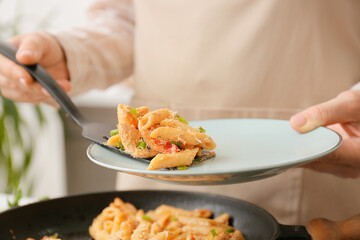 Woman putting cajun chicken pasta into plate, closeup