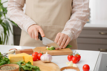 Woman cutting green onions on table in kitchen