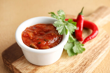 Board with bowl of tasty salsa sauce on color background