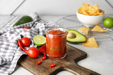 Glass jar of tasty salsa sauce with ingredients on table