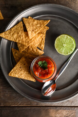 Plate with glass jar of tasty salsa sauce and nachos on wooden background