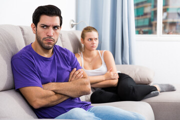 Young man sitting on sofa at home offended after quarrel with wife