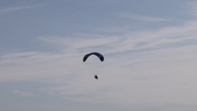 Solo Man flying to the right with powered paragliding, also known as paramotoring or PPG, as a form of ultralight aviation and the pilot wears a back-mounted motor