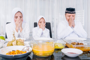 Parents and daughter praying before dinner at home