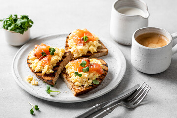 Scrambled egg sandwich with salmon on a ceramic plate on a white background, delicious and healthy breakfast, selective focus