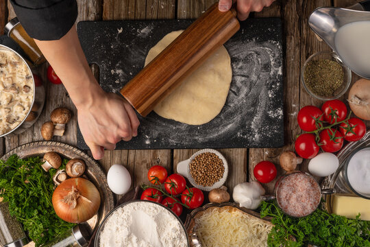 The process of kneading the dough on a background with ingredients, top view on a wooden table. The concept of making bread, italian pizza, pie or focaccia, recipe book
