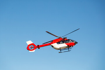 Fototapeta na wymiar Red and white fire fighter helicopter flying in the air on background of blue clear sky. High quality photo. Transportation and technology concept