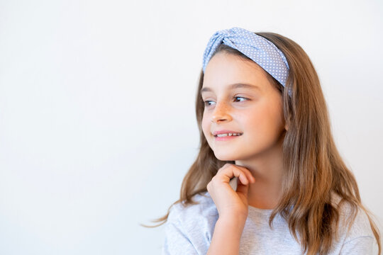 Curious child portrait. Kid fashion. Creative idea. Thoughtful inspired smiling little girl in blue polka dot hair band accessory looking at empty space isolated white advertising background.