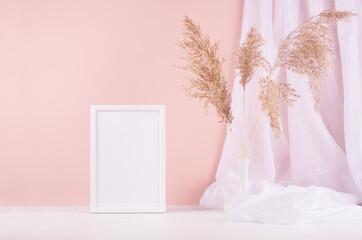 Soft pastel pink interior with blank photo frame, white silk curtain and beige fluffy reeds on wood shelf, copy space.