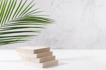 Natural wood podium with green palm leaf in white and grey marble interior with sunlight and...