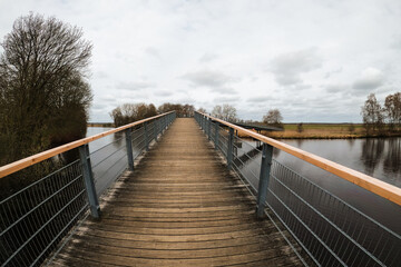 Long wooden bridge over a river on a cloudy day, wide angle