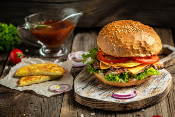 Tasty grilled homemade burgers with beef, tomato, cheese, bacon and lettuce on rustic wooden background. fast food and junk food concept