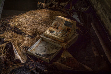A damaged cash register with some straw around in a derelict building