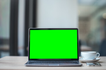 Fototapeta premium Mockup of laptop computer with empty screen with coffee cup and smartphone on table of the coffee shop background,Green screen