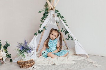 Little cute happy girl in a blue dress playing with toys in a white wigwam Close up photo of happy child. © Наталья Мокрецова