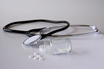 Selective Focus object. A overturned bottle of medicine and a stethescope just behind it on a white background. Space for Text.