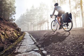 Fototapeta na wymiar Cyclist on a bicycle with panniers riding along a foggy forest road