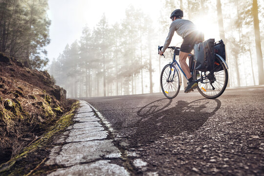 Cyclist on a bicycle with panniers riding along a foggy forest road