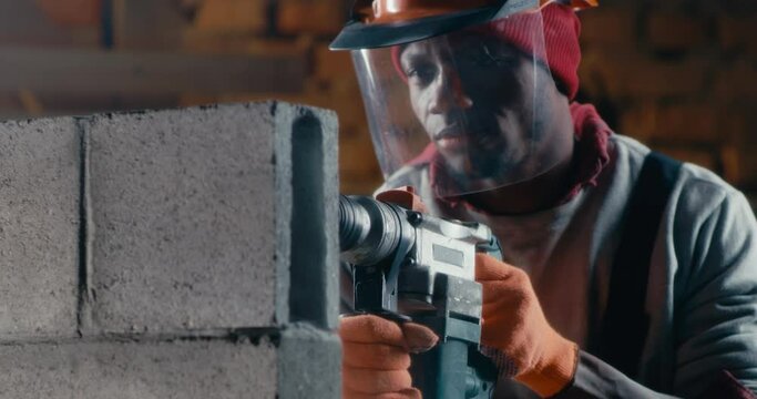 African American builder drilling brick wall