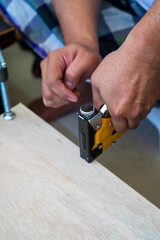 Carpenter using an industrial construction stapler on a wood plank.