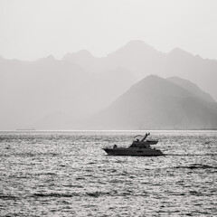 Summer landscape with views of the Mediterranean coast. Layers of mountains on the horizon, rays of the sun breaking through the clouds, silhouette of a yacht at sea. Antalya, Turkey