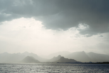 Summer landscape with views of the Mediterranean coast. Layers of mountains on the horizon, rays of the sun breaking through the clouds. Evening time before sunset. Antalya, Turkey