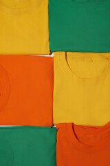 Closeup of folded colorful yellow, orange and green cotton t shirts. Flat lay tees template