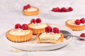 Small tartlet pastries with white cream, topped with raspberry fruits and almond sprinkles
