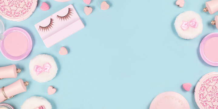 Banner with cute pink makeup beauty products like brushes, powder or lipstick on sides of pastel blue background with empty copy space in middle