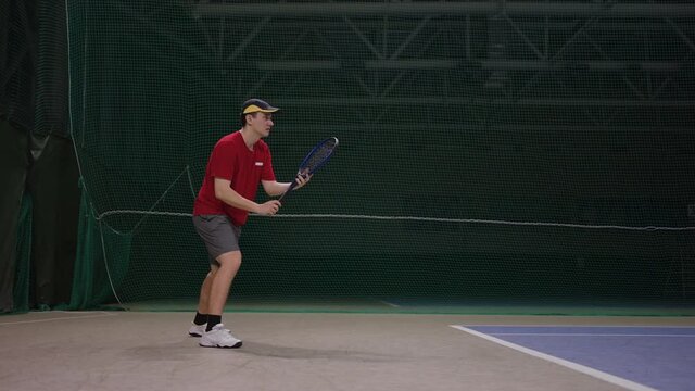adult professional tennis player is waiting serve of opponent, hitting ball by racquet on indoor court