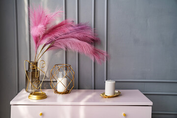 light pink dresser at the gray wall decorated with candles and colored feathers.