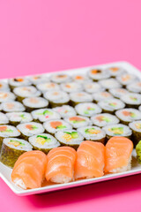 Sushi large set served on a white plate over pink background. Traditional Asian Japanese cuisine concept.