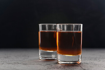 Two shot glasses with alcohol over black background. Alcoholic beverages, drinks.