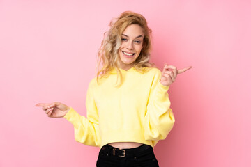 Young blonde woman wearing a sweatshirt isolated on pink background pointing finger to the laterals and happy